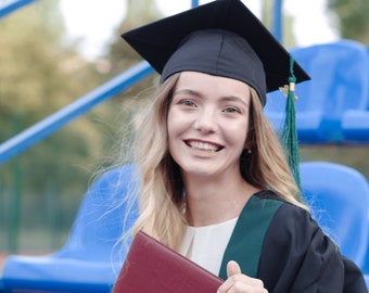 Puede incluir: Una mujer con una toga y un gorro de graduación negros sostiene un diploma rojo. Está sonriendo y sentada en una grada azul.