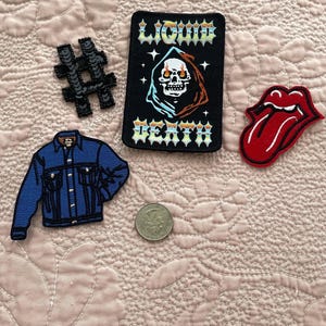 Peut inclure: Un ensemble de patchs thermocollants comprenant une veste en jean, un crâne enflammé, un hashtag et une langue rouge. Les patchs sont sur un fond de tissu matelassé rose.