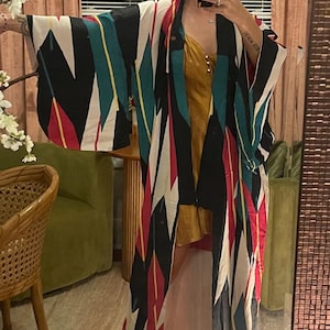 Könnte beinhalten: Ein schwarz-weißes Kimono mit roten, gelben und blauen geometrischen Mustern. Das Kimono wird über einem goldenen Schlupfkleid getragen.