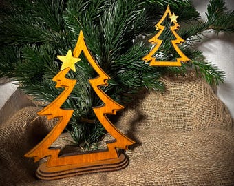 May include: Wooden Christmas tree ornaments with a star on top. The ornaments are a warm brown color and are set against a backdrop of evergreen branches and burlap fabric. The ornaments are approximately 4 inches tall.