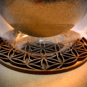 May include: A wooden coaster with a geometric pattern, resembling a flower of life design, is shown with a clear glass cup on top.