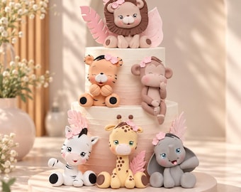 May include: A two-tiered cake decorated with fondant animal figurines including a lion, tiger, monkey, zebra, giraffe, and elephant. Each animal features small pink flower accents and is positioned on a light-colored, gradient-frosted cake base.