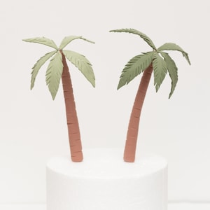 May include: Two green palm tree cake toppers with brown trunks. The palm trees are made of fondant and are perfect for a tropical themed cake.