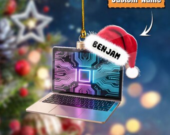May include: A laptop Christmas ornament with a circuit board design on the screen. The ornament has a Santa hat with the name "BENJAM" and the text "Custom Name". The laptop is silver and has a gold string for hanging.