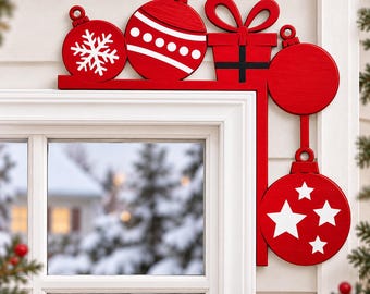 May include: A red wooden corner decoration for a window frame featuring three round ornaments with white snowflake, dot, and star patterns, along with a red gift box with a black ribbon design, all arranged in a festive holiday-themed display.