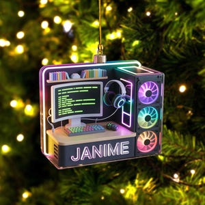 May include: A computer-themed Christmas ornament featuring a desk, monitor, keyboard, and headphones. The ornament has a black and neon-lit design, with the name "JANIME" displayed on the front. The computer fans have a rainbow color scheme.