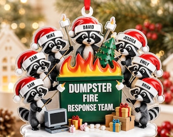May include: A Christmas ornament featuring seven raccoons wearing Santa hats, each with a name tag. They surround a green dumpster labeled DUMPSTER FIRE RESPONSE TEAM with flames on top. The raccoons hold sticks with marshmallows near the fire.