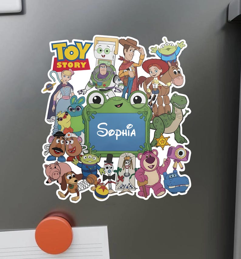 Puede incluir: Un im&aacute;n decorativo con un collage colorido de personajes de Toy Story que rodean un marco central con forma de rana verde con el nombre Sophia impreso en blanco. El dise&ntilde;o incluye a Woody, Buzz Lightyear, Jessie, Rex y otras figuras.