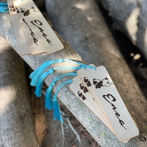 May include: A set of four wooden bookmarks featuring a panda bear design and the name "Emea" inscribed on each. The bookmarks have blue tassels.