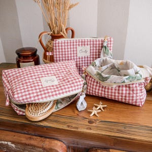 Può includere: Tre pochette trapuntate con motivo a quadretti rossi e bianchi e un'etichetta bianca con la scritta Comfy. Le borse presentano cerniere dorate, una fodera interna floreale, una spazzola per capelli in legno e due piccole stelle marine.