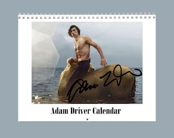May include: A wall calendar titled Adam Driver Calendar featuring a photograph of a shirtless person with dark hair sitting on a light-colored horse in the ocean. A black signature is overlaid on the image, and the calendar has a white spiral binding.