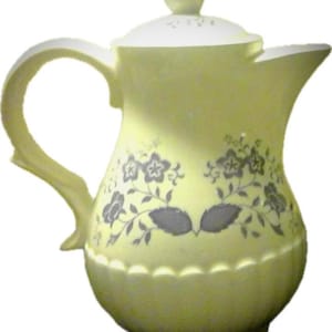 May include: A yellow ceramic teapot with a floral design in grey. The teapot has a lid and a handle.