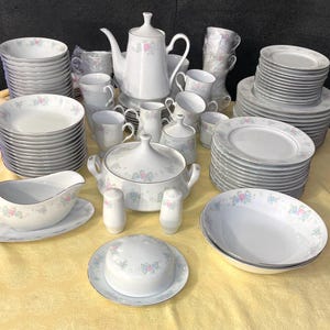 May include: A set of white porcelain dinnerware with a floral pattern in pink, blue, and green. The set includes plates, bowls, cups, saucers, a teapot, and a gravy boat.