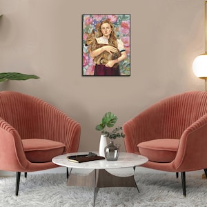 May include: A framed art print depicts a woman holding a fawn against a floral background. The artwork features a color palette of pink, brown, and white. Two coral-colored armchairs are in the foreground, with a white marble table and a gold lamp.