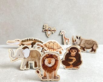 Puede incluir: Un conjunto de figuritas de animales de madera, que incluyen un león, un elefante, un rinoceronte, un cocodrilo, una tortuga, un mono y una jirafa. Las figuritas están pintadas en colores realistas y tienen un estilo caprichoso y de dibujos animados.
