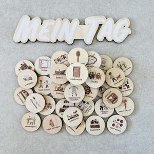Könnte beinhalten: Ein Set aus Holzscheiben mit Illustrationen von täglichen Aktivitäten wie Zähneputzen, Essen und Schlafen. Die Scheiben sind unter einem Holzschild mit dem weißen Text "MEIN TAG" angeordnet.