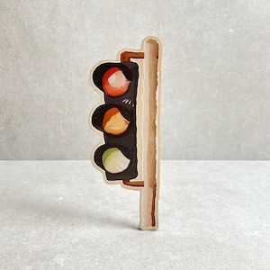 Pode incluir: Um semáforo de madeira com um poste castanho e caixas de luz pretas. A luz superior é vermelha, a luz do meio é laranja e a luz inferior é verde. A obra de arte tem uma aparência pintada à mão.