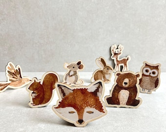 Puede incluir: Un conjunto de figuritas de animales de madera, que incluyen un zorro, una ardilla, un búho, un oso, un conejo, un pájaro y un ciervo. Las figuritas están pintadas en tonos marrones, naranjas y blancos, y tienen un estilo caprichoso y de dibujos animados.