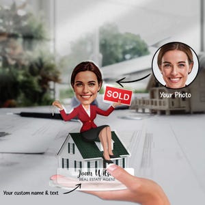 May include: A caricature of a real estate agent holding a red "SOLD" sign, sitting on a small house model. The agent is wearing a red blazer and black skirt. The agent's photo is in the top right corner. The text "Your Photo" is below the photo. The text "Joan Wils, REAL ESTATE AGENT" is on the base of the house model.