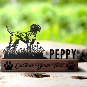 Könnte beinhalten: Schwarze Metallsilhouette eines Deutsch Kurzhaar-Hundes, der in hohem Gras steht. Der Hund steht auf einem Holzsockel mit dem Namen "PEPPY" und dem Text "Custom Your Text" mit Pfotenabdrücken auf beiden Seiten.