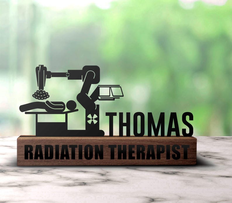 May include: A wooden plaque with a black metal cutout of a radiation therapy machine and a patient lying on a table. The plaque reads "Radiation Therapist" and "THOMAS".