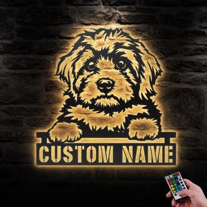 May include: A black metal silhouette of a dog's head with the text "CUSTOM NAME" below. The silhouette is illuminated with warm white light. A remote control with multiple colored buttons is visible in the bottom right corner.