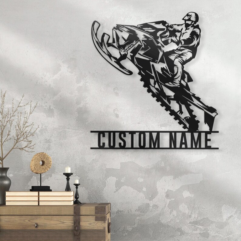 Puede incluir: Arte de pared de metal negro con una moto de nieve con un conductor, con el texto "CUSTOM NAME" debajo.