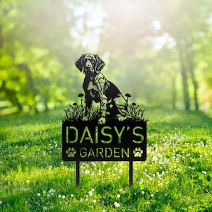 Puede incluir: Señal de jardín de metal negro con una silueta de un perro sentado en un lecho de hierba. El letrero dice "Daisy's Garden" con huellas de patas a cada lado de la palabra "Garden".