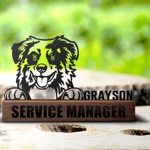 May include: A black and white silhouette of a dog with a happy expression, peeking over a wooden sign that reads "GRAYSON SERVICE MANAGER".