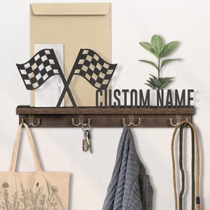 May include: A wooden wall-mounted organizer with a shelf, hooks, and a decorative racing flag design. The shelf features the text "CUSTOM NAME" and holds a small plant and mail. A tote bag, keys, and a scarf hang from the hooks.