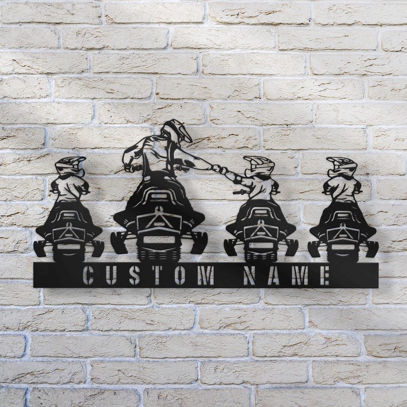 May include: Black metal silhouette of four people riding snowmobiles. The snowmobiles are in a line, with the person in the front leading the way. The silhouette is mounted on a black metal plaque with the text "CUSTOM NAME" below it.
