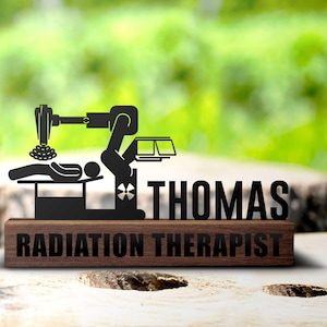 May include: A wooden plaque with a black metal cutout of a radiation therapy machine and a patient lying on a table. The plaque reads "Thomas Radiation Therapist".
