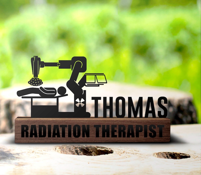 May include: A wooden plaque with a black metal cutout of a radiation therapy machine and a patient lying on a table. The plaque reads "Thomas Radiation Therapist".