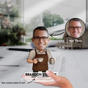 May include: A personalized barista figurine with a cartoon-style illustration of a man wearing glasses and an apron, holding a coffee cup and a pitcher. The base reads "BRANDON STE... BARISTA" with space for custom text. A photo is included.
