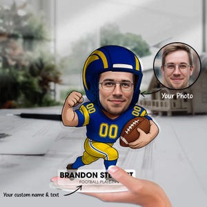 Könnte beinhalten: Personalisierte Footballspieler-Figur mit individuellem Foto. Die Figur zeigt eine Cartoon-Illustration eines Footballspielers in blau-gelber Uniform, der einen Football hält. Der Text "BRANDON STEWART FOOTBALL PLAYER" wird auf der Basis angezeigt.