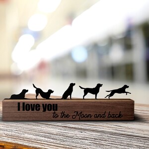 Può includere: Un cartello di legno con cinque silhouette di cani neri in varie pose. Il cartello dice "Ti amo fino alla luna e ritorno".