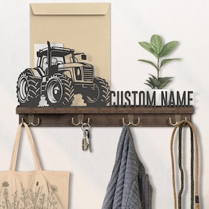 Puede incluir: Estante de pared de madera marrón oscuro con una silueta de tractor y las palabras "CUSTOM NAME". El estante tiene cuatro ganchos de latón, una pequeña planta y un sobre beige.