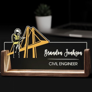 Peut inclure: Plaque de bureau en bois avec un fond noir. La plaque porte le nom "Brandon Jonhson" et le titre "CIVIL ENGINEER" en écriture blanche. Un graphique d'un pont et d'un ingénieur est sur le côté gauche.