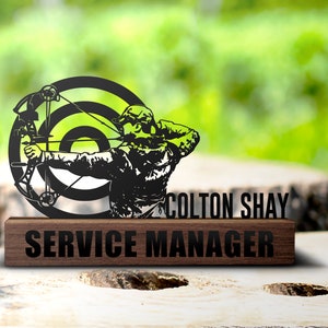 Peut inclure: Silhouette noire en métal d'un archer visant une cible avec le texte "COLTON SHAY SERVICE MANAGER" sur une plaque en bois.
