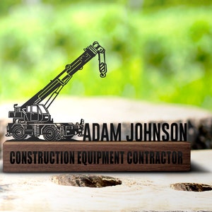 Könnte beinhalten: Schwarze Metallkran-Silhouette auf einem Holzsockel mit dem Text "ADAM JOHNSON CONSTRUCTION EQUIPMENT CONTRACTOR".