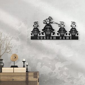 May include: Black metal wall art featuring four snowmobile riders, with the text "CUSTOM NAME" below.