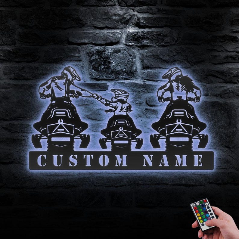 May include: A metal silhouette of three people riding snowmobiles with the text "CUSTOM NAME" below. The silhouette is lit up with a white light.
