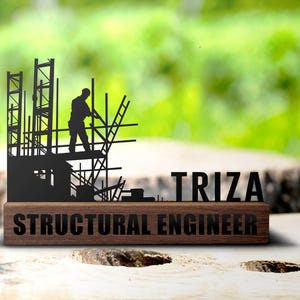 Puede incluir: Una silueta negra de metal de un trabajador de la construcción en un andamio, con el texto "TRIZA STRUCTURAL ENGINEER" en una base de madera.