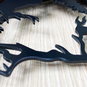 May include: Black metal silhouette of a deer with antlers, cut out and mounted on a wood background.
