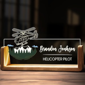 May include: A wooden desk nameplate with a helicopter design and the name "Brandon Johnson, Helicopter Pilot" in white script. The design includes a mountain scene with trees and clouds, and the nameplate is illuminated.