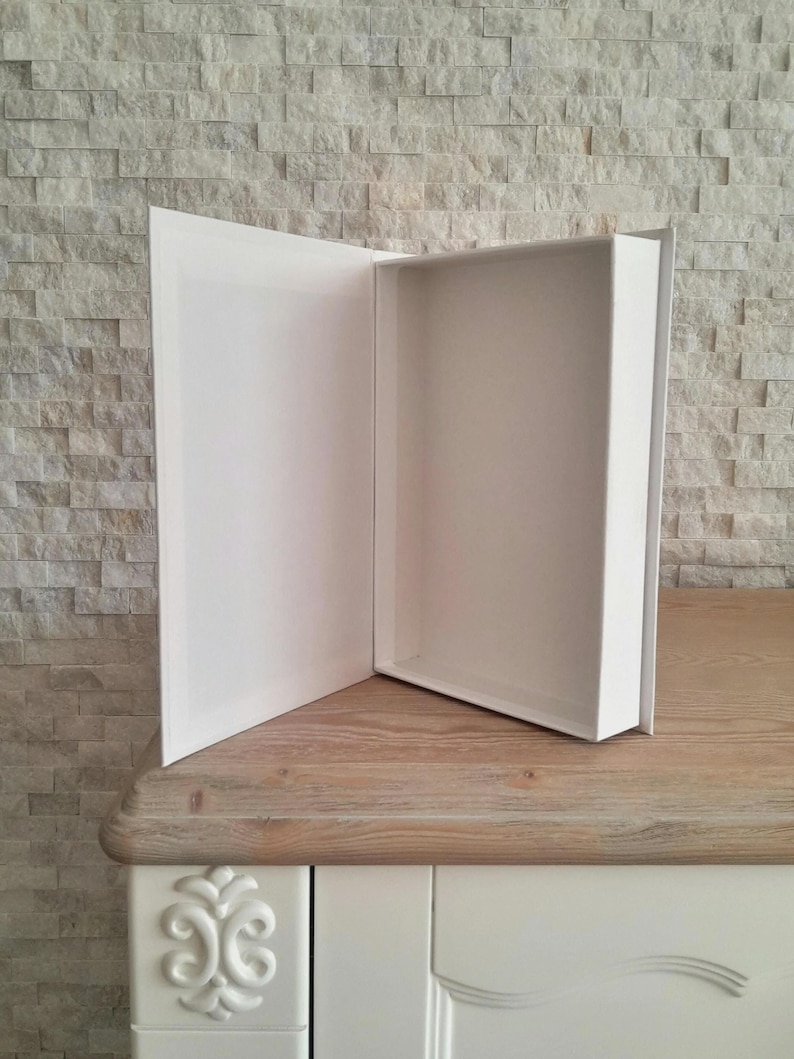 May include: A white cardboard box with a hinged lid is open, revealing an empty interior. The box is sitting on a light brown wooden surface.