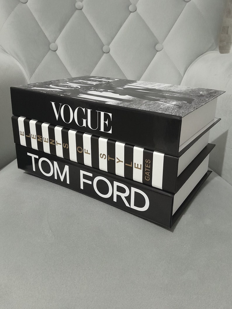 May include: A stack of three black and white hardcover books with gold lettering. The top book says "VOGUE", the middle book says "Elements of Style", and the bottom book says "TOM FORD".