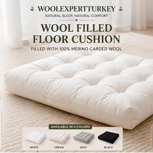 Peut inclure: Un coussin de sol carré blanc cassé rempli de laine cardée 100 % mérinos et recouvert d'une housse en coton durable. Le coussin présente un design capitonné et est accompagné de texte détaillant ses matériaux naturels, sa fabrication artisanale et sa disponibilité en quatre couleurs : blanc, crème, gris et noir.