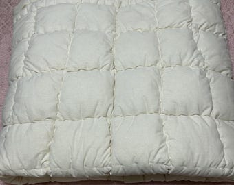 May include: A white quilted bed topper with a square pattern. The topper is folded in half and is lying on a pink patterned bedspread.