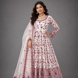 Puede incluir: Traje Anarkali bordado floral blanco y burdeos con dupatta a juego. El vestido de manga larga presenta intrincados patrones florales y una silueta acampanada. El dupatta tiene un borde a juego. El conjunto se combina con pantalones blancos y zapatos dorados. El texto "IndianSareeDesign" es visible.
